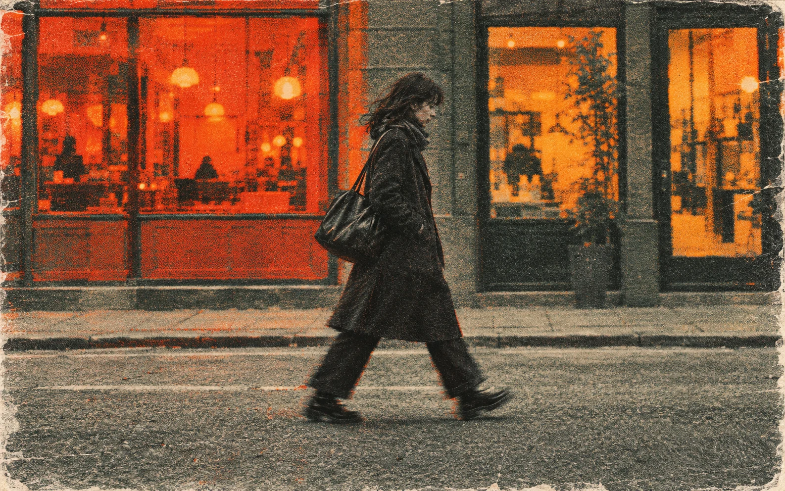 A person in a dark coat walking across a street in front of a glowing orange storefront