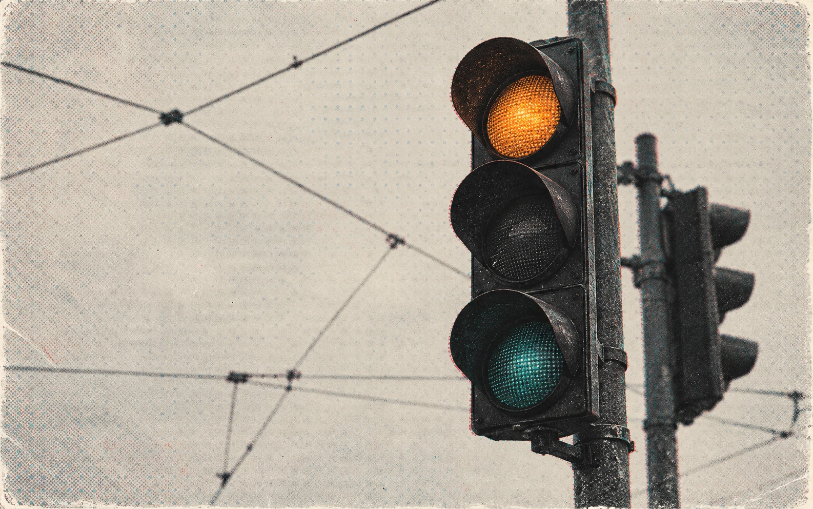 A traffic light glowing amber against a pale sky with overhead wires